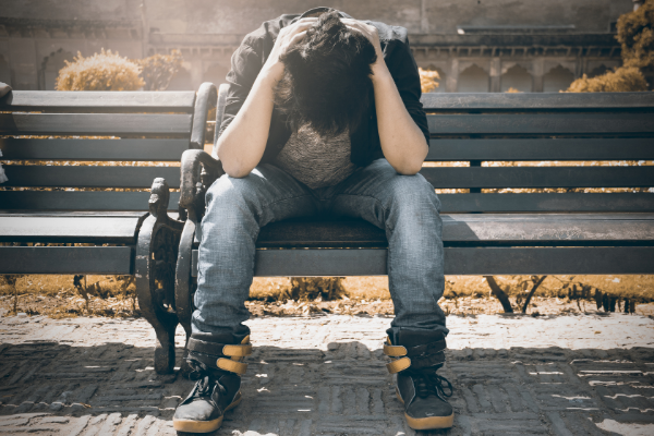 A man sat on a park bench with his head in his hands. 