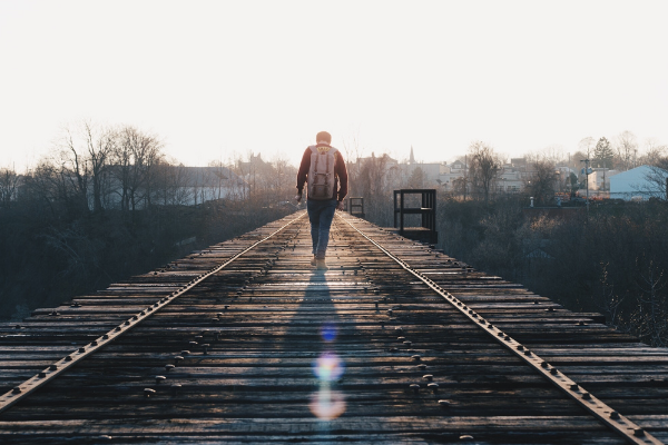 A picture of a man walking down a old wooden structure that sort of looks like an old railway track.